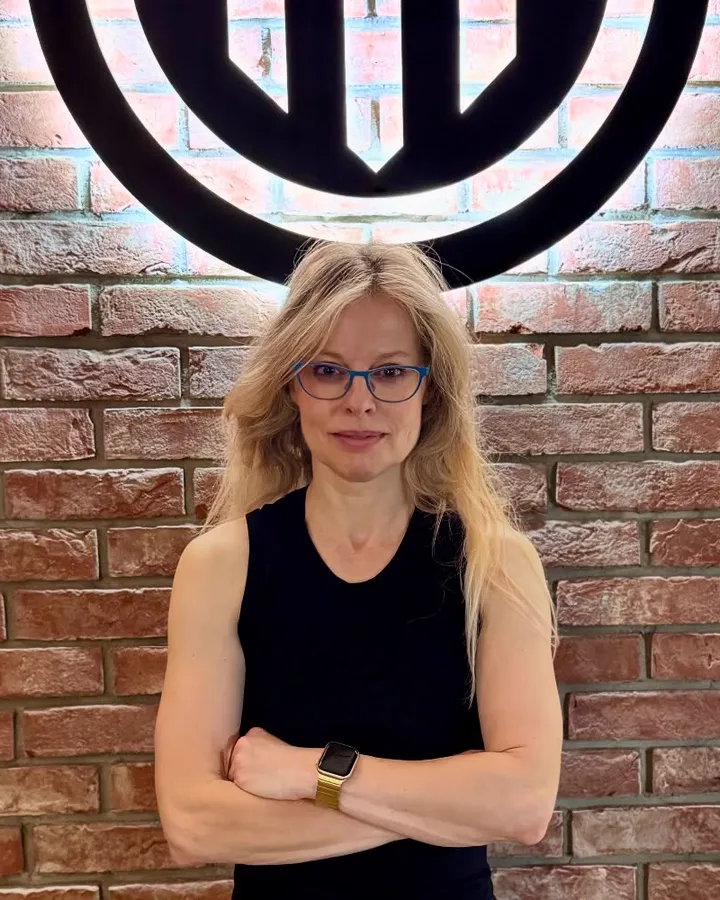 Martina se založenýma rukama u cihlové zdi s logem fitka